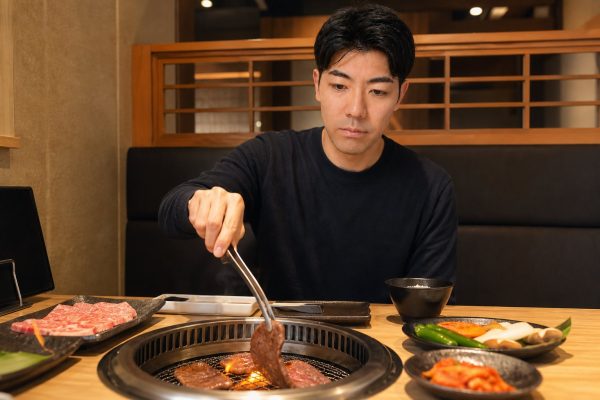 焼肉店で網の肉を焼く男性